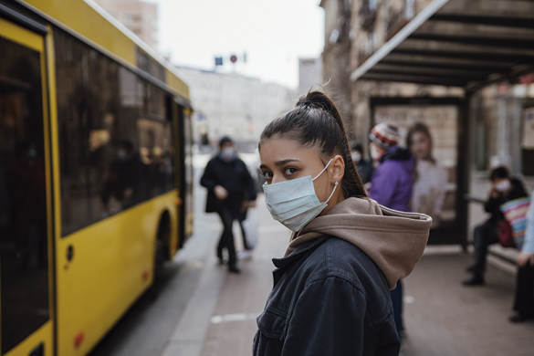 Young woman wearing surgical mask outdoor at bus stop in the street