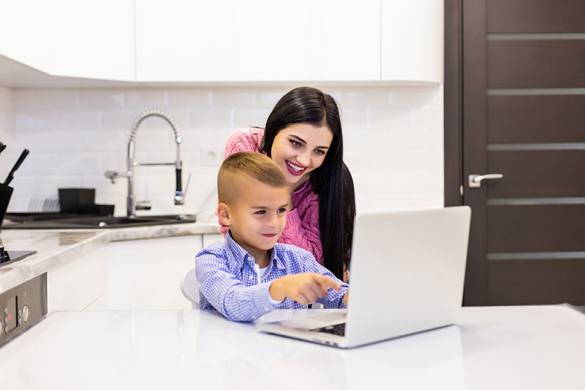 Mother overlooks as her son uses his laptop to study in their kitchen